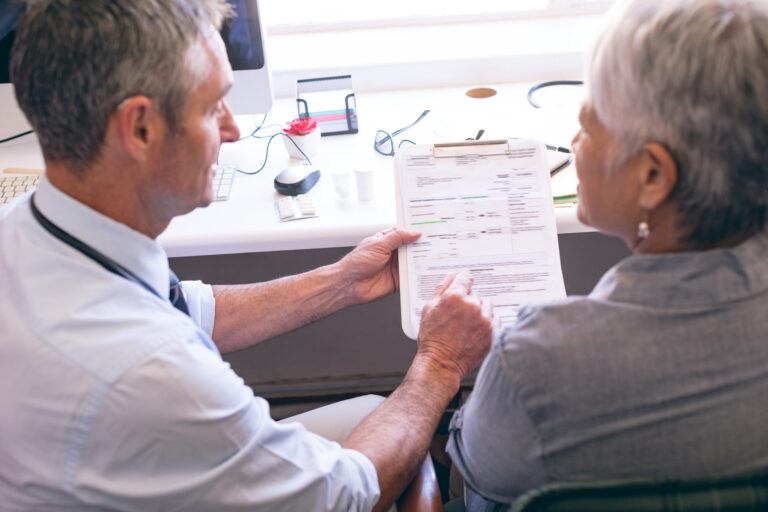 front view of matured Caucasian male doctor showing medical report to the senior mixed race female patient at clinic at retirement home