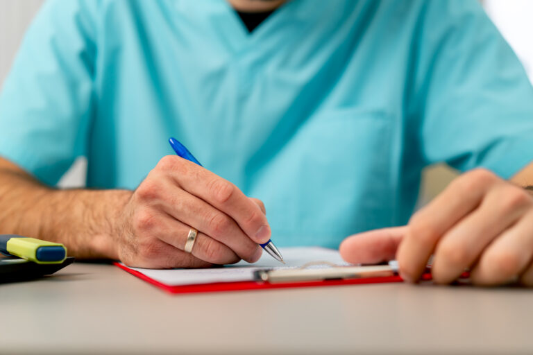Close-up shot of a male doctor's hand with a ring on his finger filling out a patient's medical history
