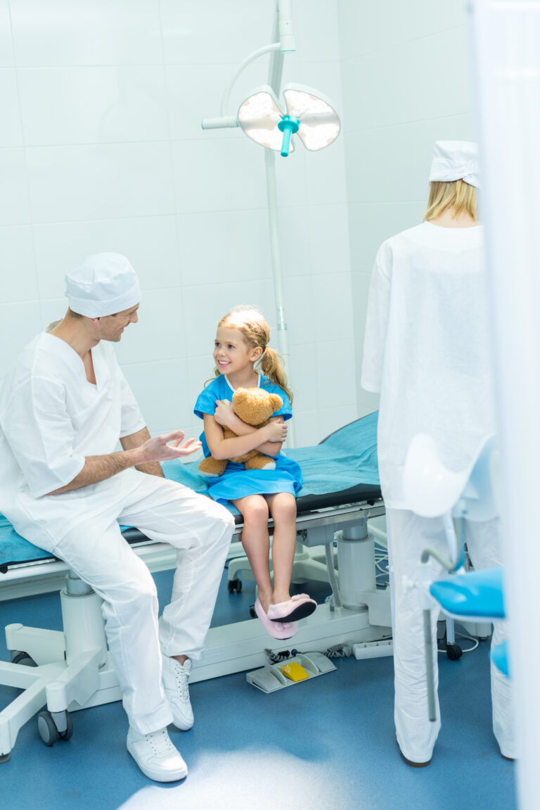 doctors preparing smiling kid for surgery in operating room